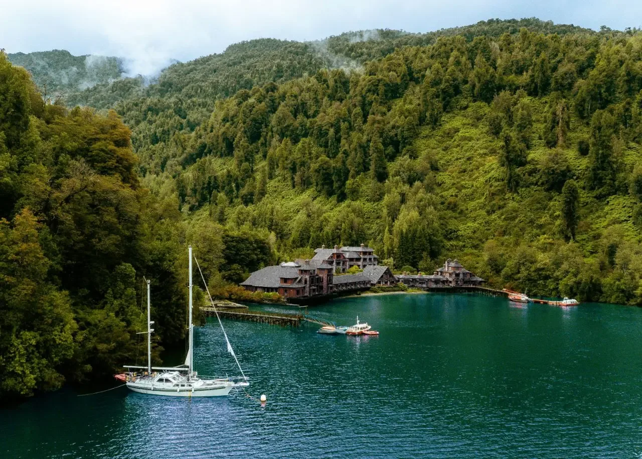 A boat is moored beside a low lodge on a green Patagonian fjord.