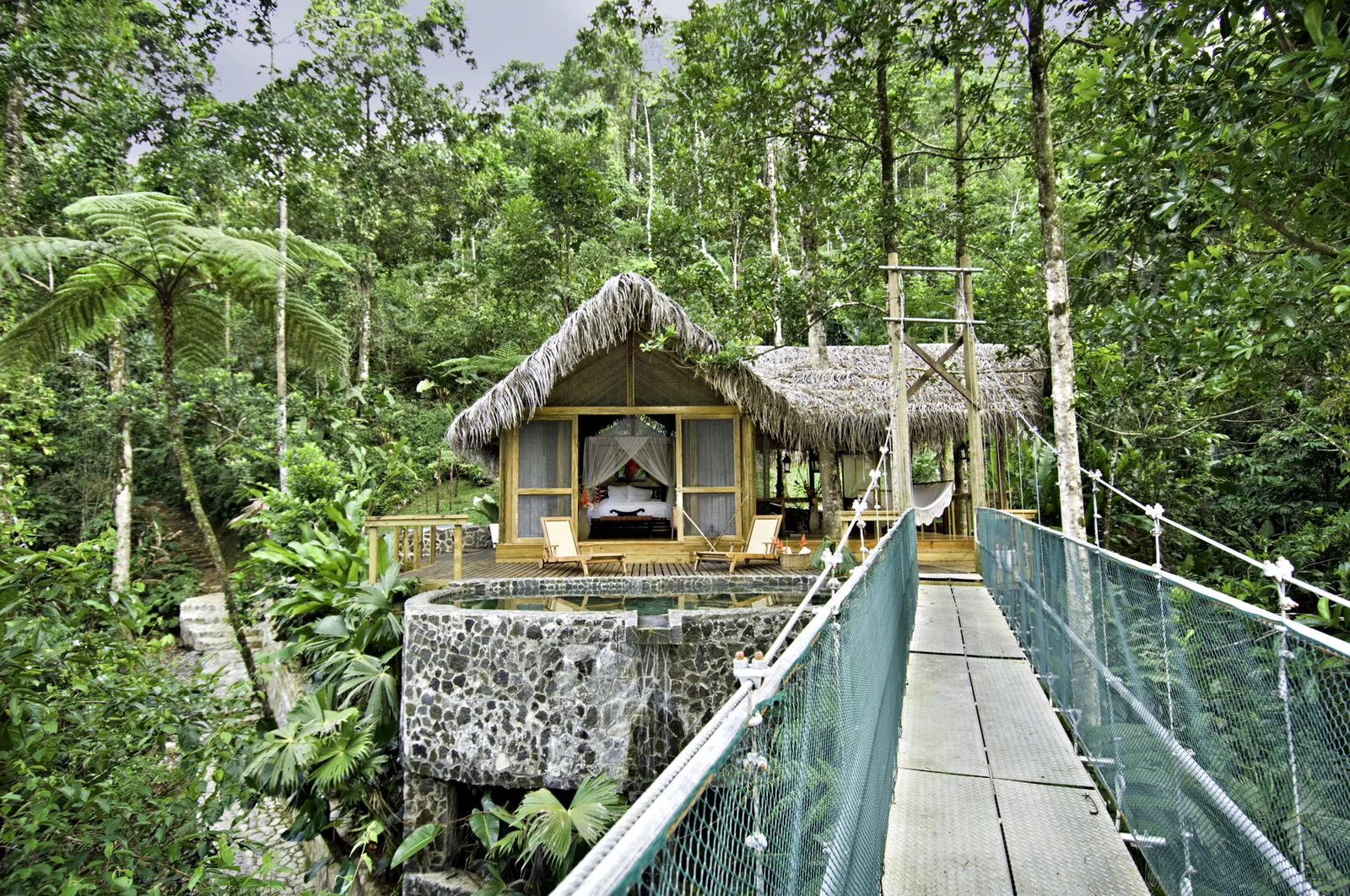 A wooden lodge and suspended walkway are nestled in dense rainforest.