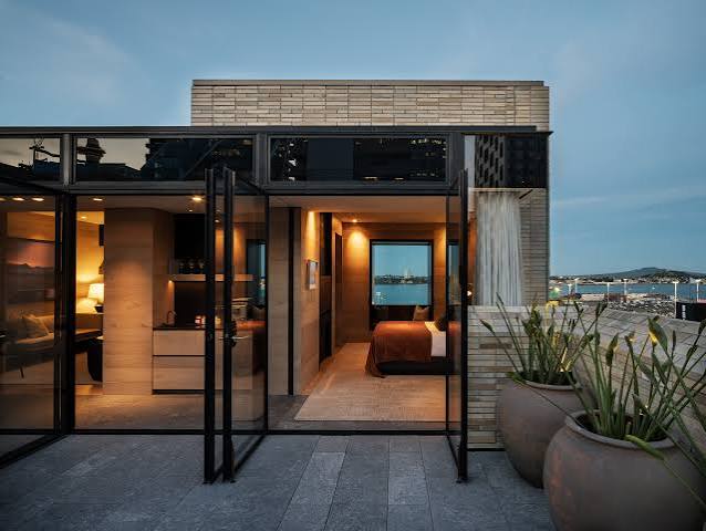 A suite at The Hotel Britomart opening onto a planted terrace with views toward Auckland's waterfront at dusk.