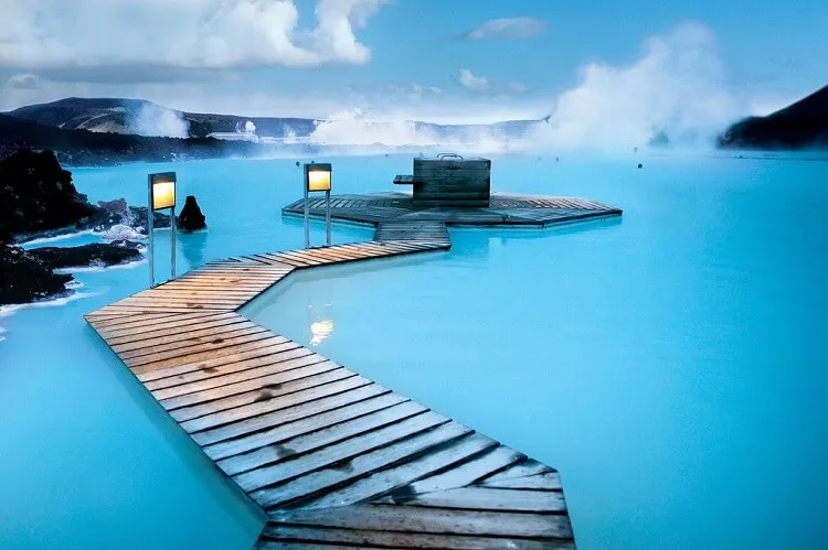 Turquoise geothermal water beside a dark lava-rock shore at Iceland’s Blue Lagoon.