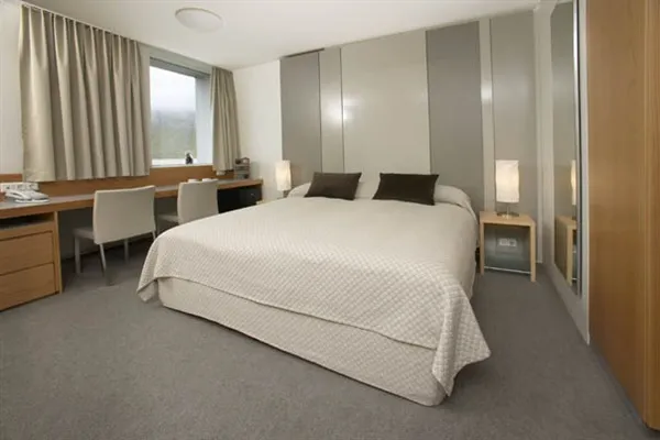 A simple hotel bedroom with a double bed, wardrobe, and desk.