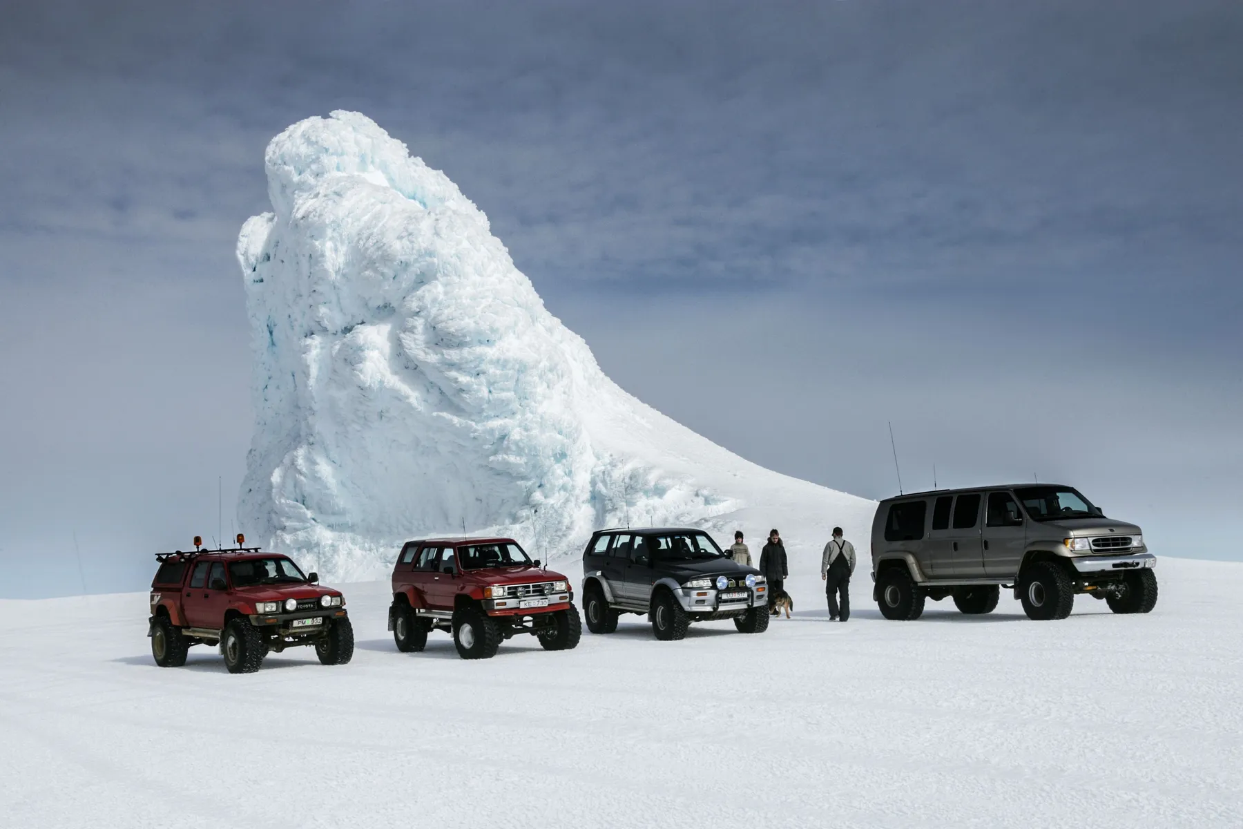 Four-wheel-drive vehicles crossing a snowy Icelandic glacier landscape.