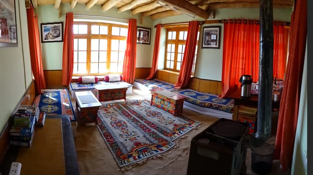 A guest bedroom in a Ladakhi lodge, with carved wooden furniture and a red patterned rug.