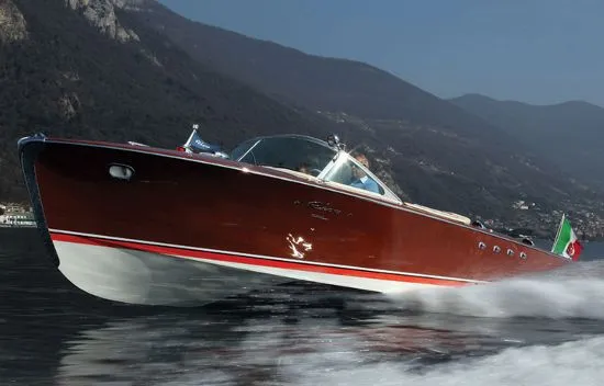 A classic wooden motorboat cruising on Lake Como beside a mountainous shore.