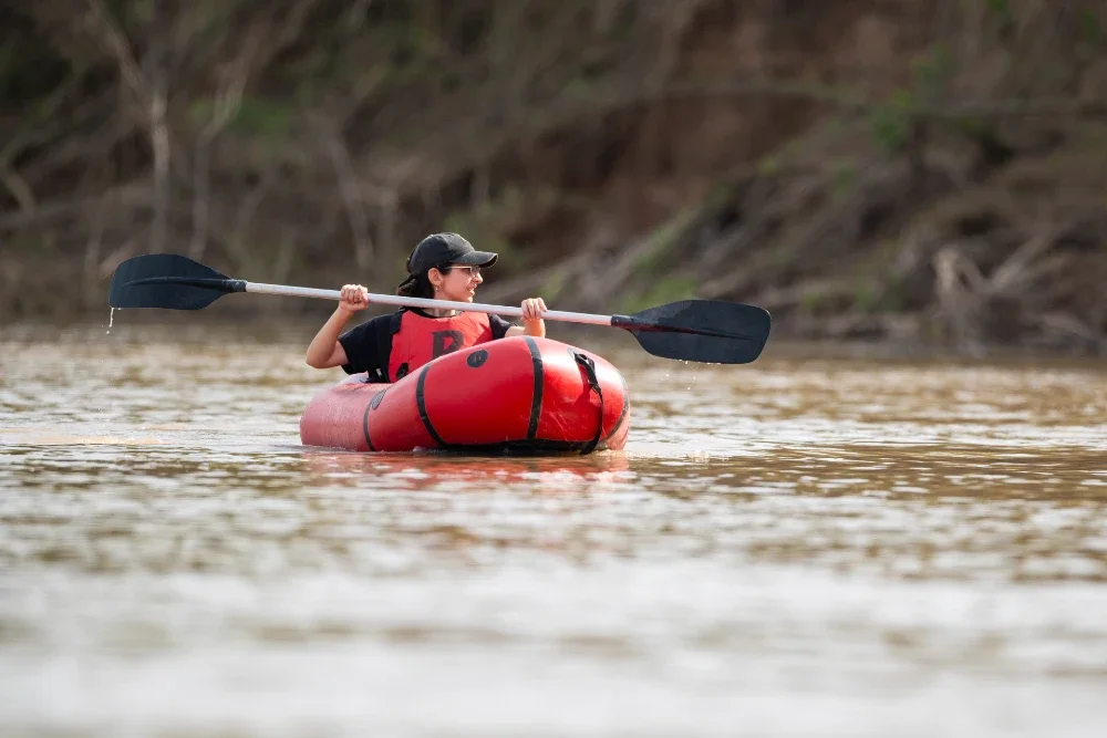 A person paddling a red kayak along a river.