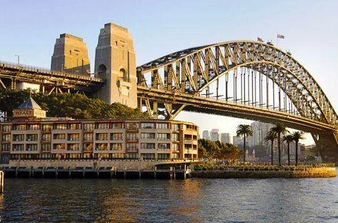 Sydney Harbour Bridge above waterfront buildings and blue water.