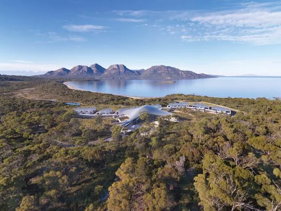 Aerial view of a lodge amid coastal bushland with mountains and water beyond.