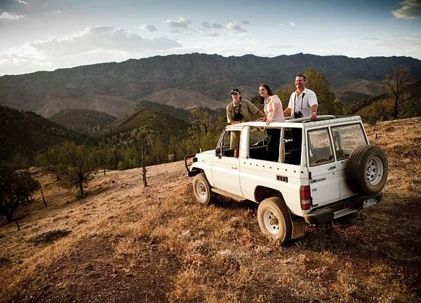 Guests looking out from a four-wheel-drive vehicle on a ridge above rugged hills.