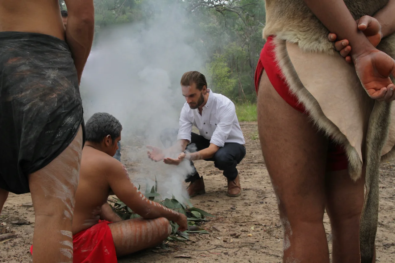 People gathered outdoors around a small smoking fire.