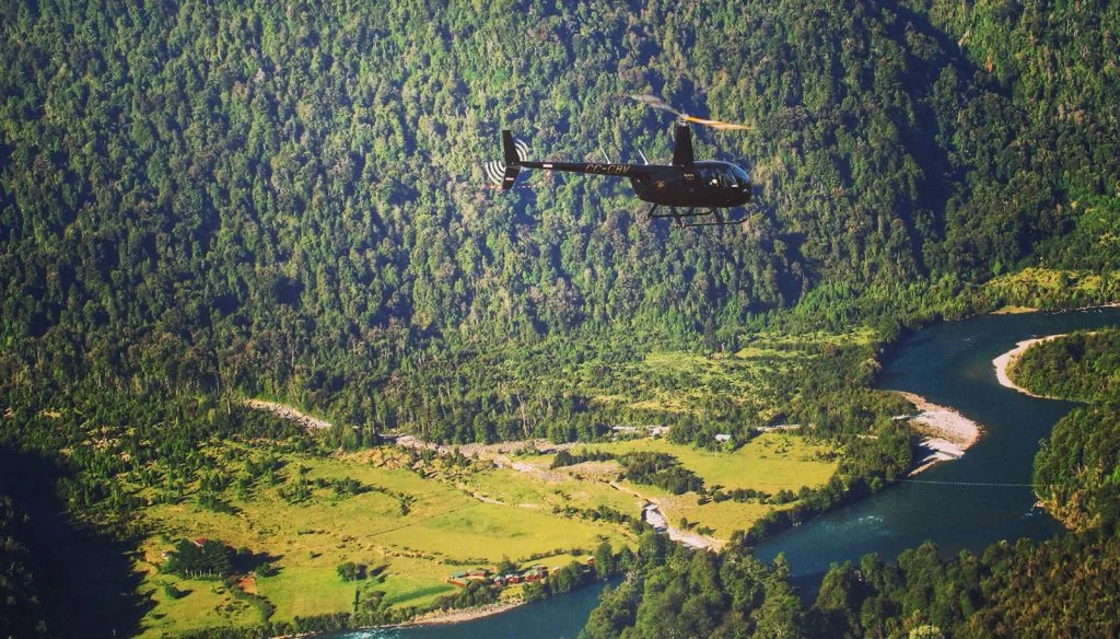 A helicopter flying above a forest beside a winding river.