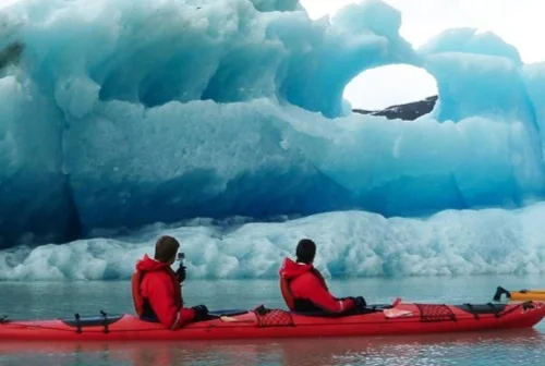 Two people in a red kayak beside a blue iceberg.