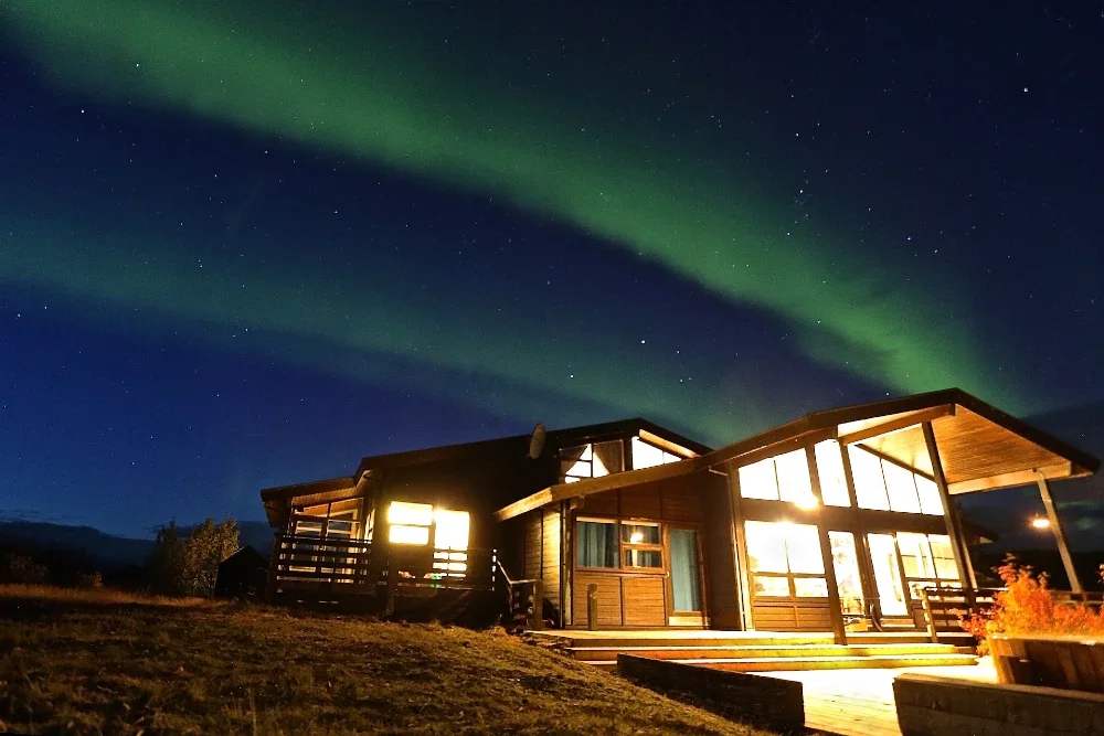 A brightly lit house beneath green northern lights in a dark night sky.