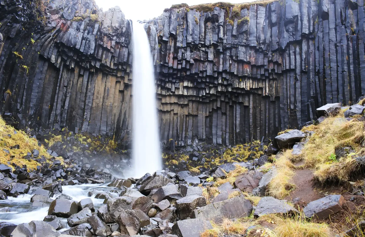 A waterfall cascading over dark basalt columns into a rocky basin.