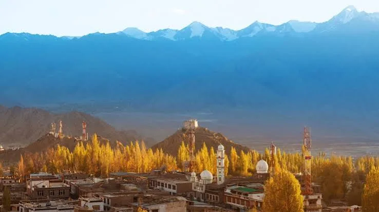 A settlement among golden autumn trees beneath a broad mountain range.
