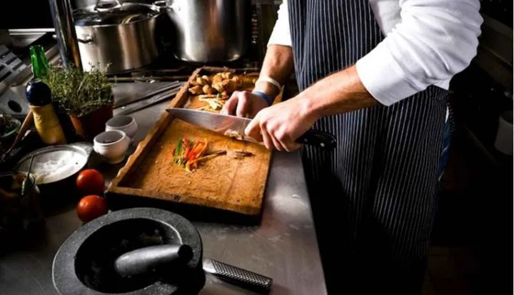 A cook preparing food on a wooden chopping board in a kitchen.