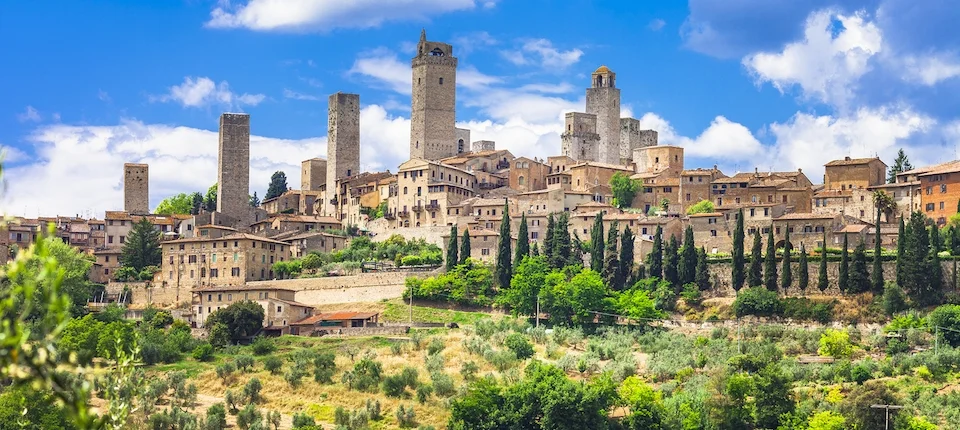 Medieval stone towers rising above a Tuscan hill town and green countryside.