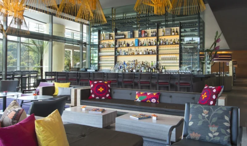 A bright lounge and bar with colourful cushions and large windows.