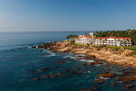 White resort buildings with red roofs overlooking a rocky coastline and blue ocean.