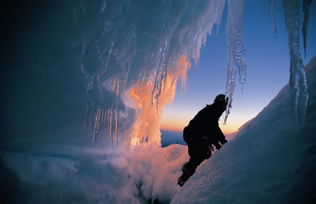 A person standing inside a blue ice cave illuminated by warm light.