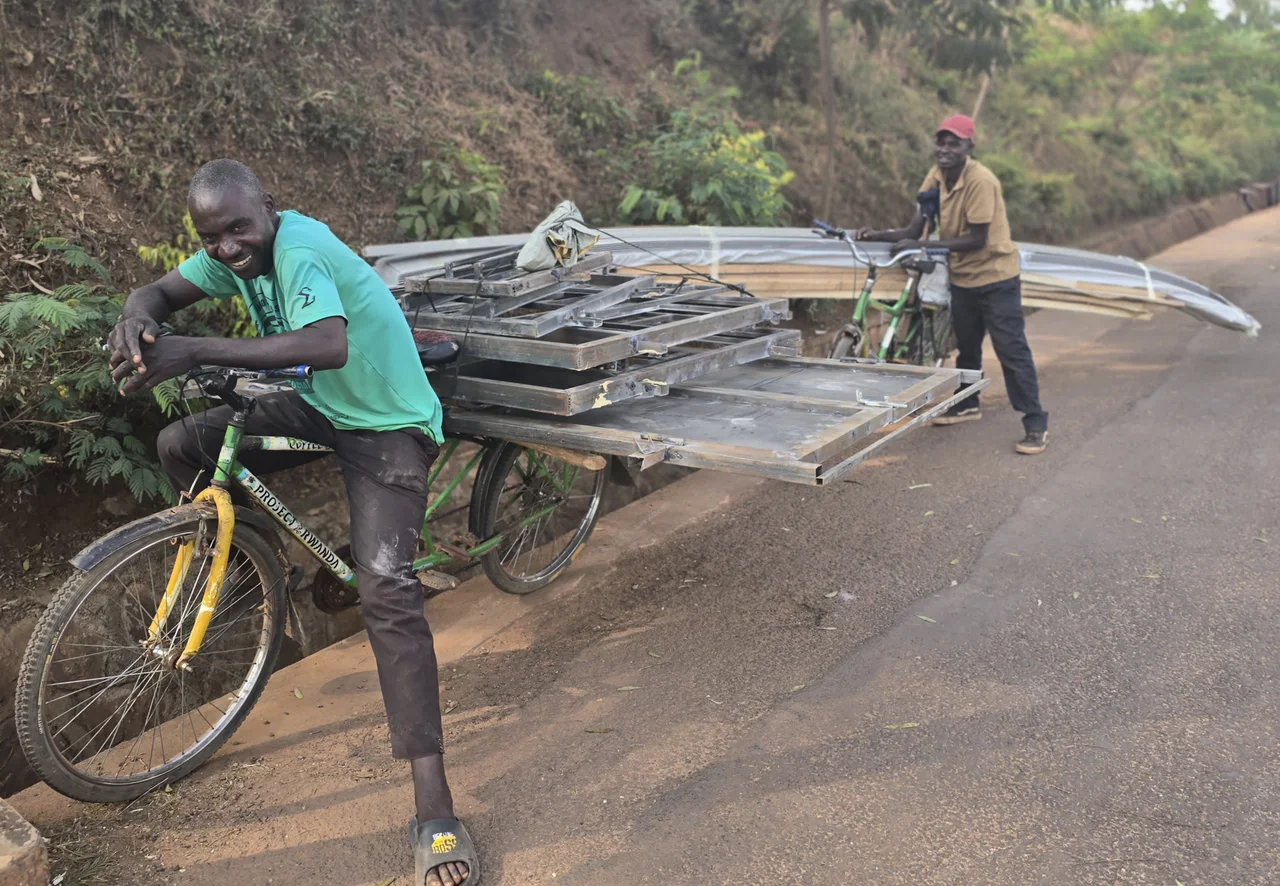Two people pushing bicycles loaded with large frames along a roadside.