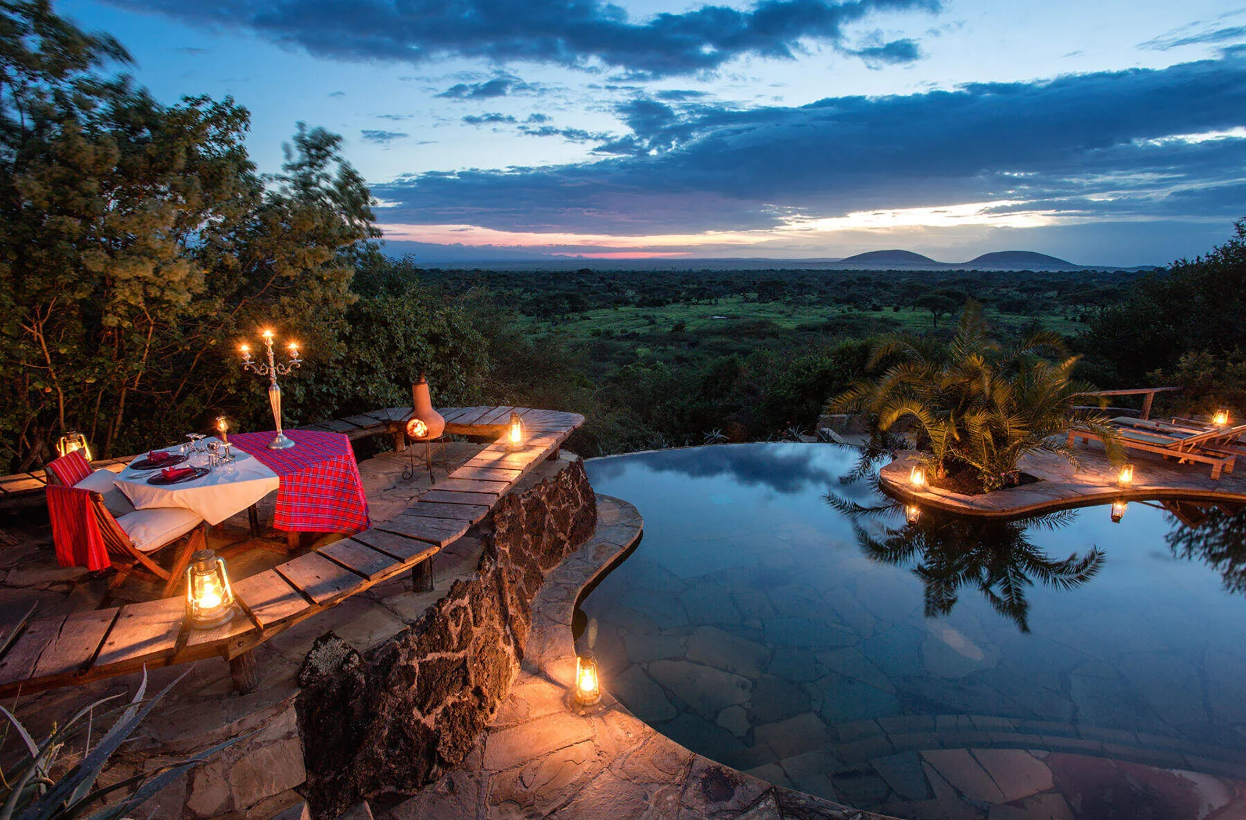 A candlelit table and pool overlook an open landscape at dusk.