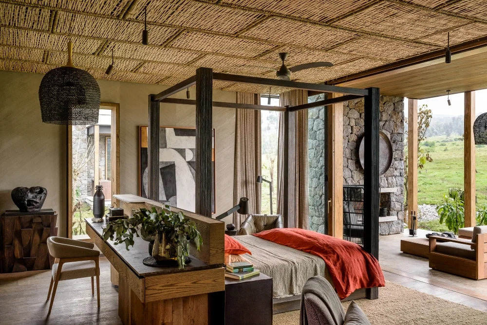 A bedroom at Kataza House with timber furnishings, stone walls and broad windows opening onto greenery.