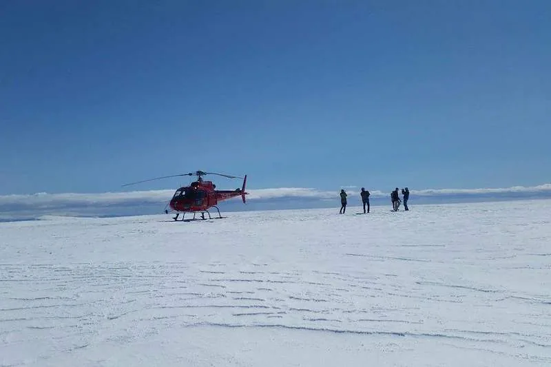 A red helicopter rests on a snow-covered Icelandic glacier as visitors stand nearby.