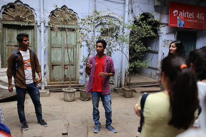 A group walks through a narrow Delhi lane beside old shopfronts.