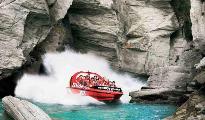 Visitors ride a red jet boat through a narrow rocky river gorge.